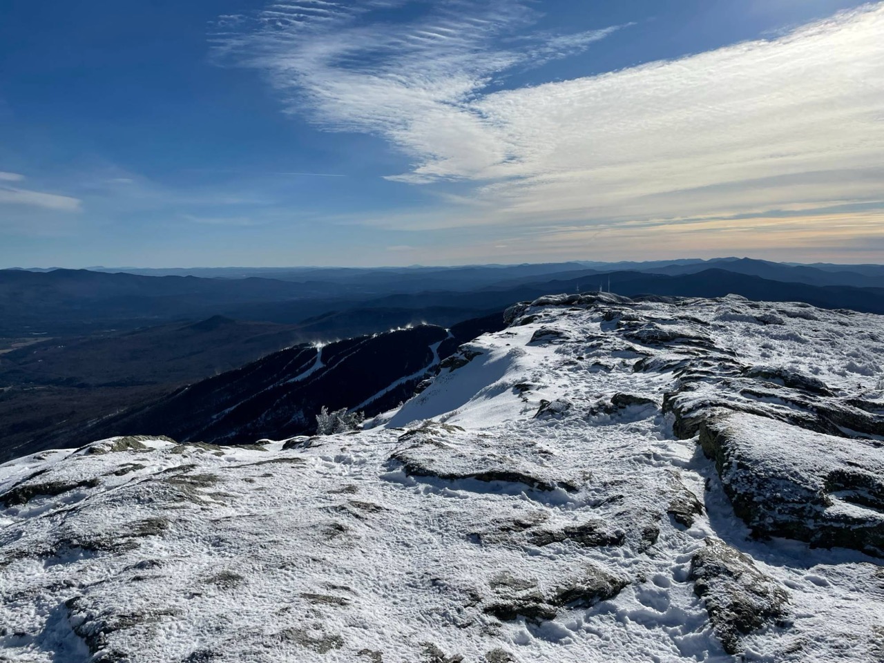 Snow-covered rocky summit of Mount Mansfield with ski trails and rolling mountains below