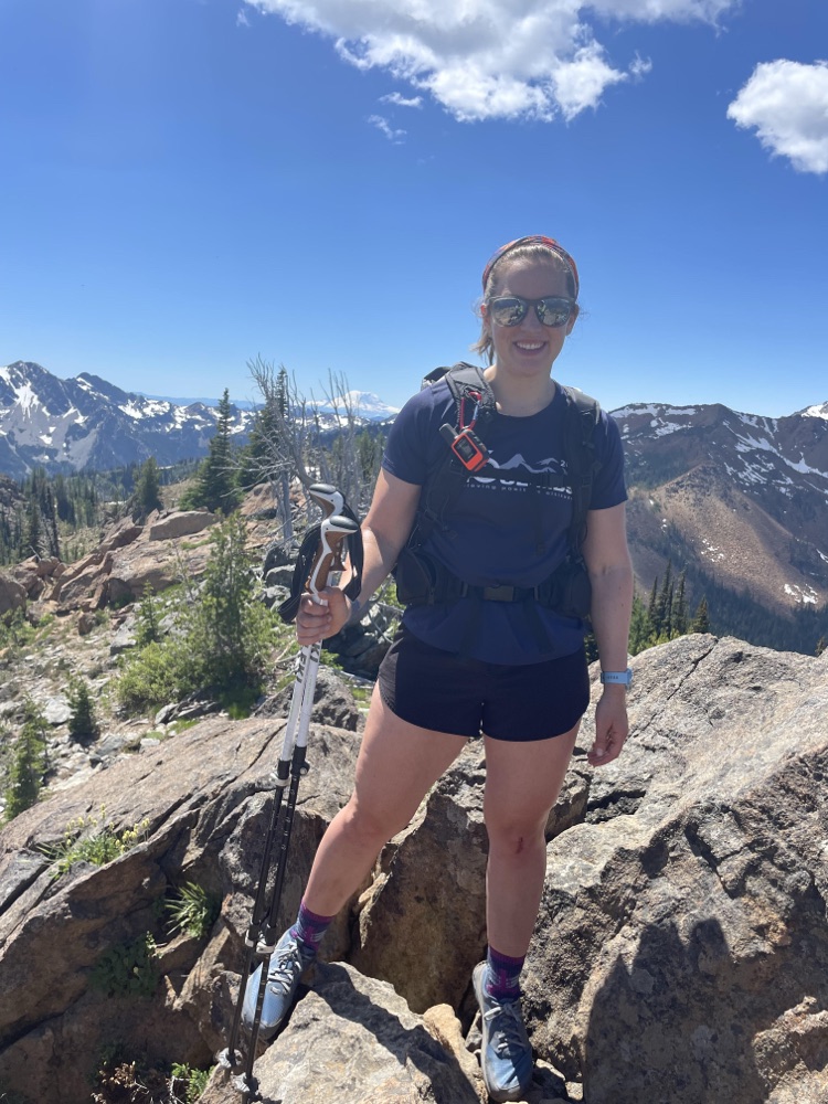 Mariah on a rocky summit with snowy mountains behind her